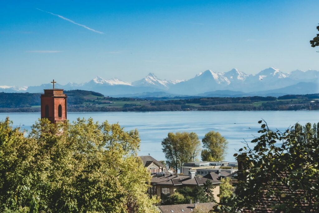 Blick von Neuenburg über den Neuenburgersee auf die verschneiten Alpen, links ein roter Kirchturm