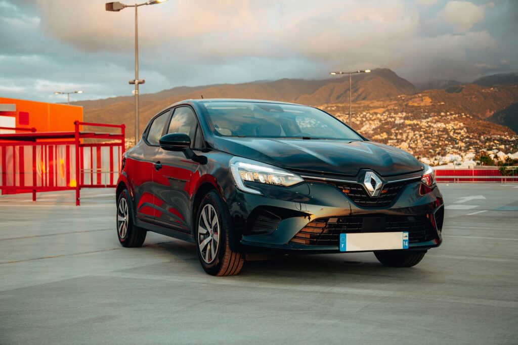 Renault Clio foncée sur un parking à étages, avec des collines dans la lumière du soir en arrière-plan