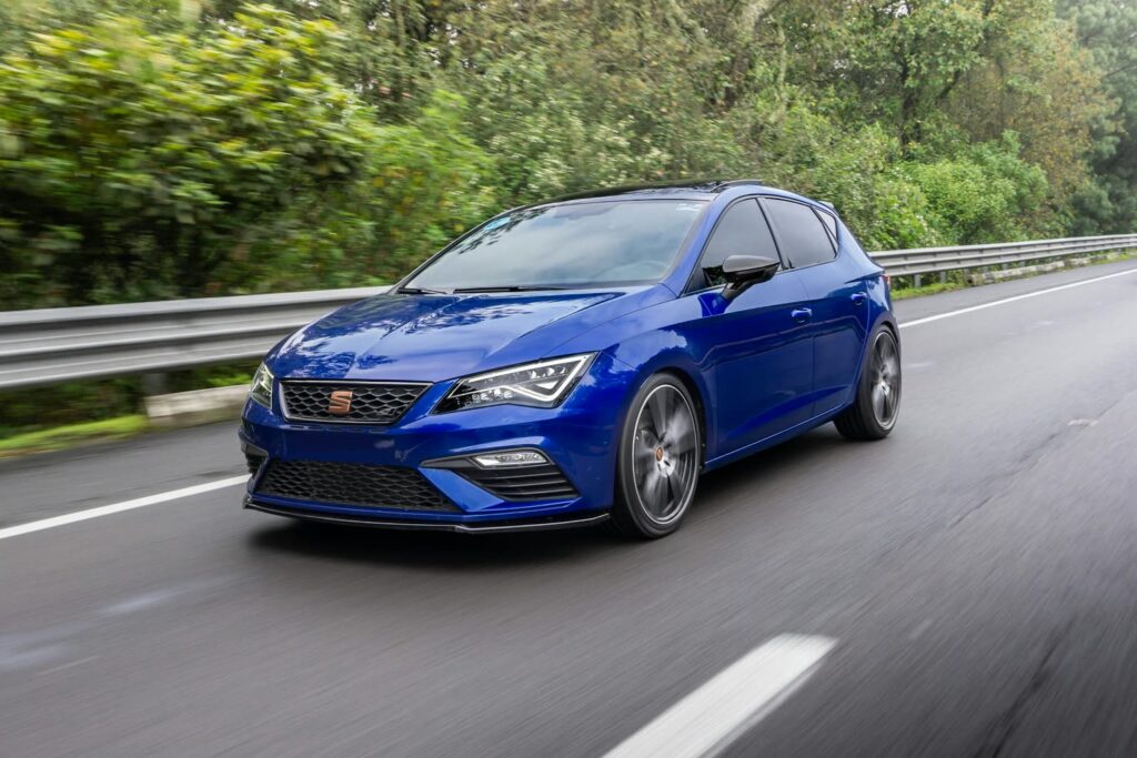 Blauer Seat Leon in Fahrt auf einer Landstrasse vor grünen Bäumen
