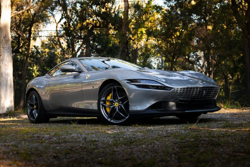 Silberner Ferrari Roma auf einem Kiesplatz am Waldrand
