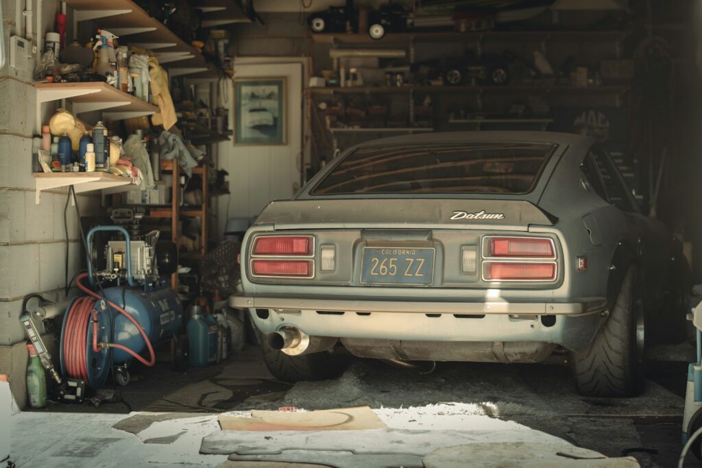 An older car in a garage full of tools and shelves