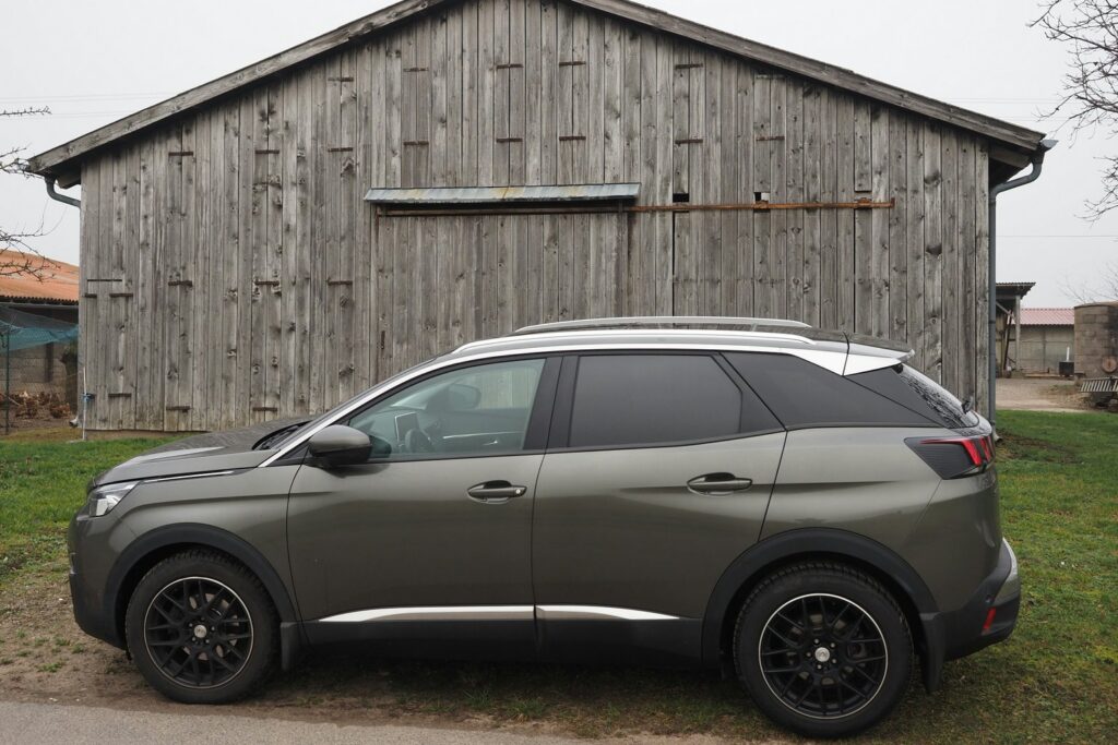 Grauer Peugeot 3008 von der Seite auf einer Wiese vor einer alten Holzscheune