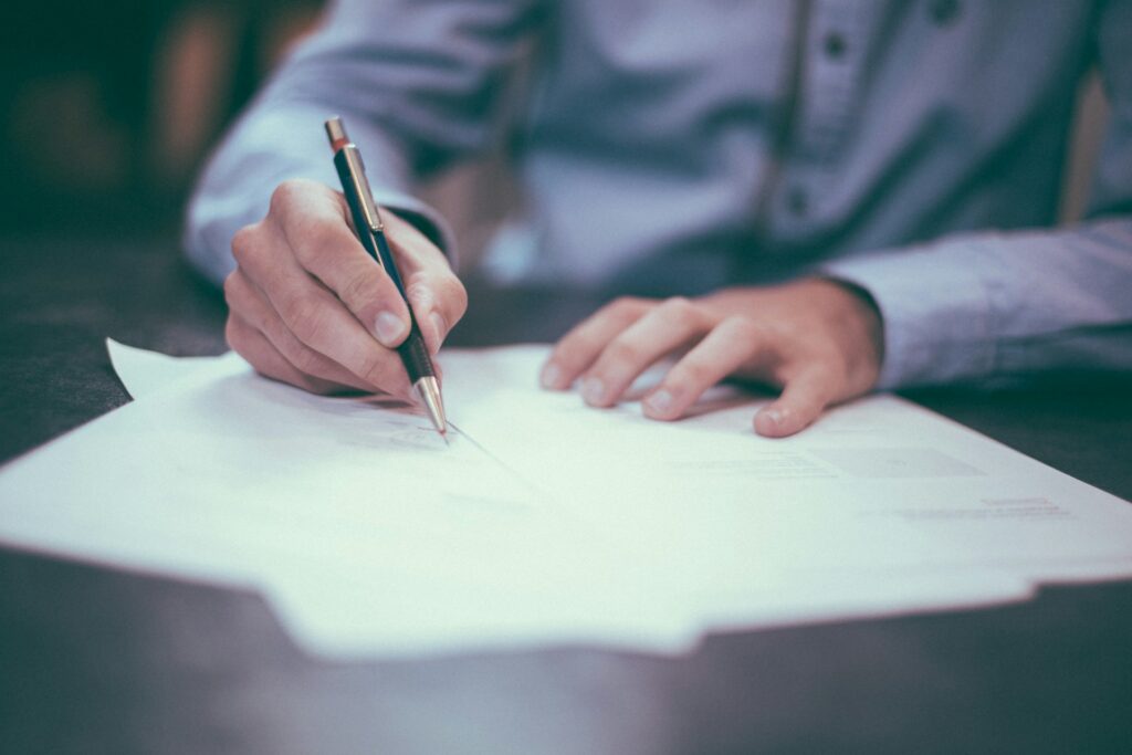 A person signing a document with a ballpoint pen